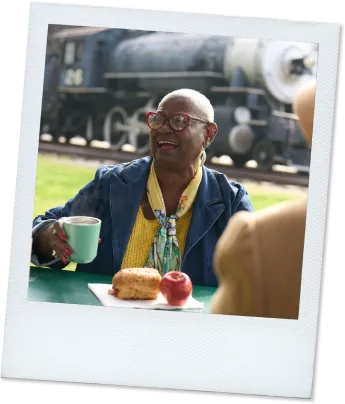 Polaroid of Joy, a real TAVR patient, enjoying a picnic lunch outdoors with a train in the background